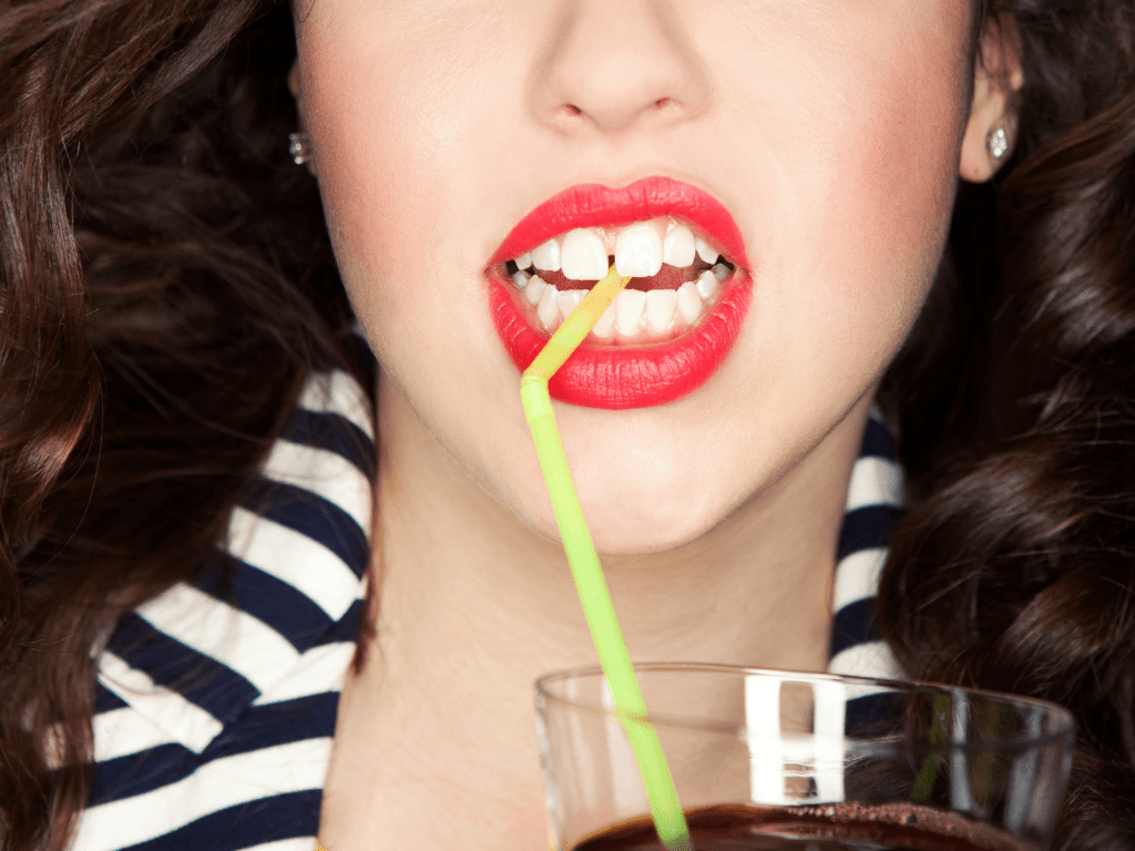 gura de femeie careia i se vad dintii cu strungareata in timp ce suge dintr-un pai