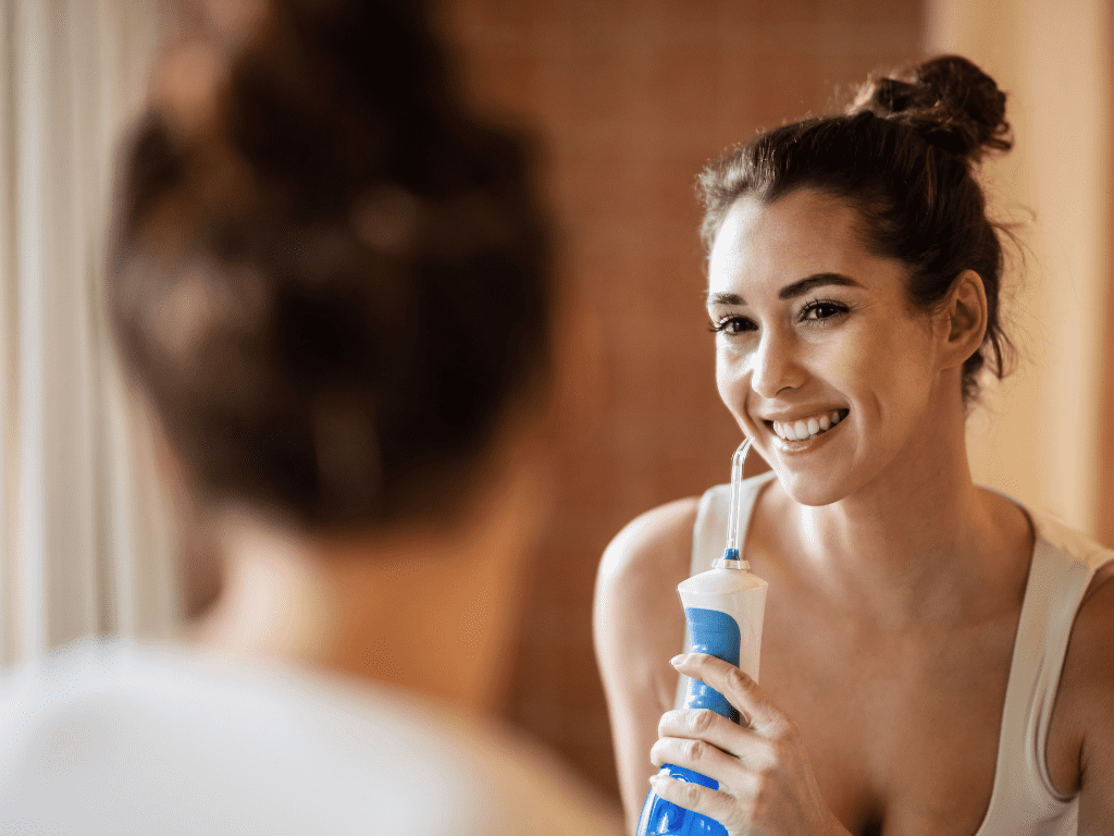 femeie care isi curuta dintii cu ajutorul unui irigator oral