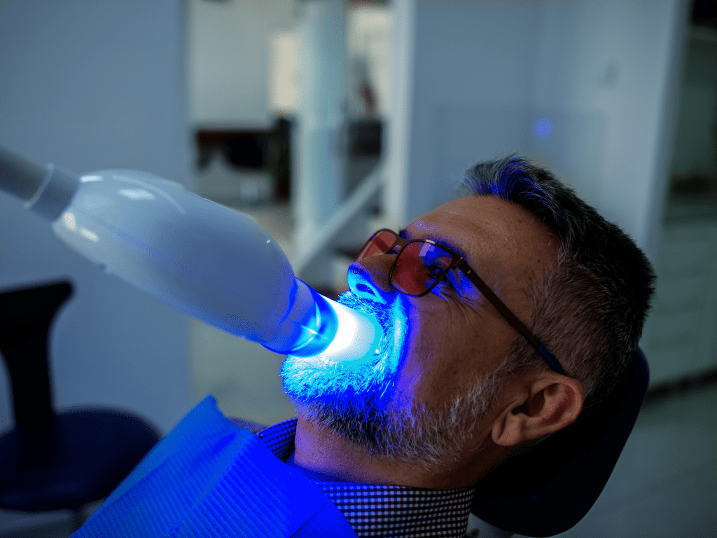 pacient barbat care isi face tratament de albire a dintilor cu lampa polarizanta