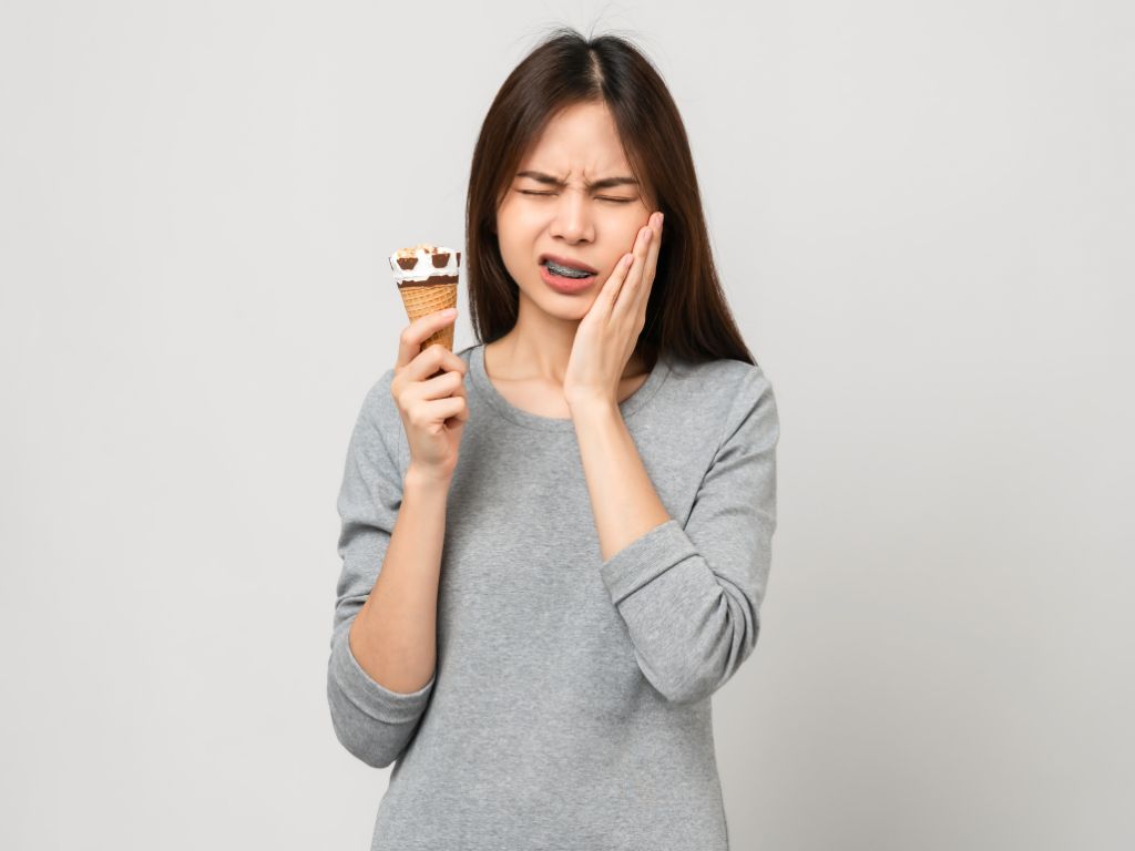 femeie cu aparat dentar care mananca inghetata si are durere de dinti
