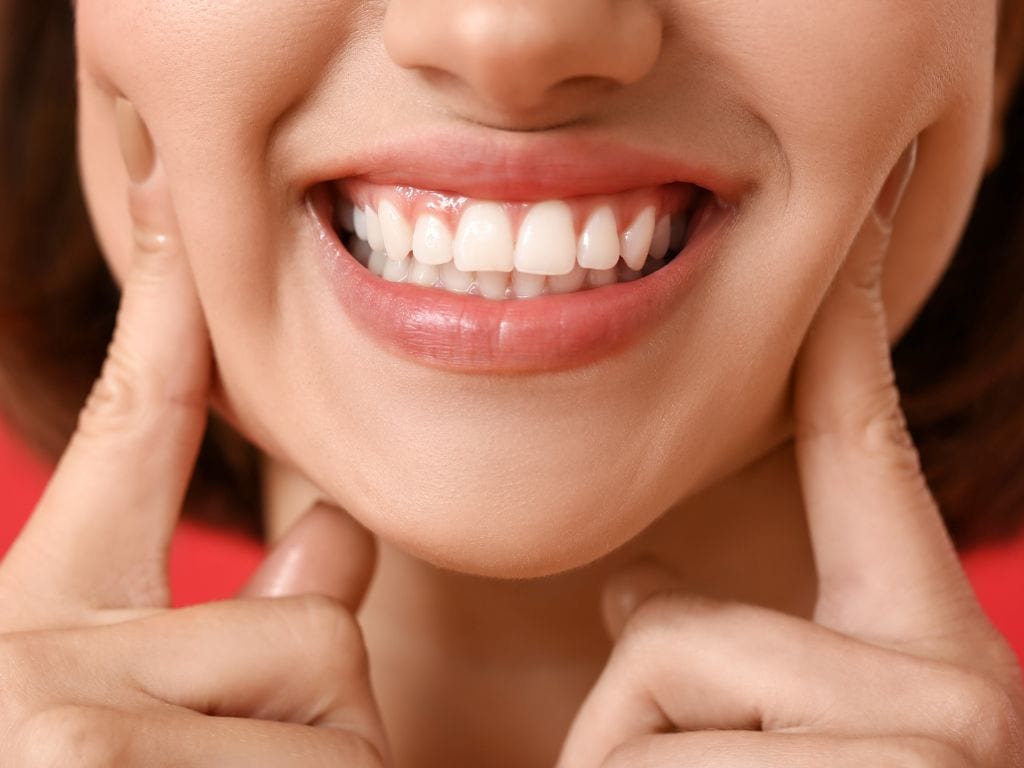 femeie cu dinti albi si drepti care tine degetele aratatoare pe obraji